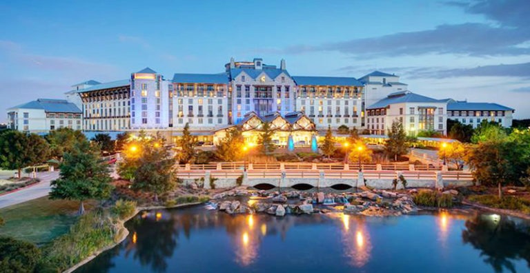 This is an image of the Rosewood Mansion on Turtle Creek. The front of the hotel is visible, and a beautiful lake nearby is visible as well. 